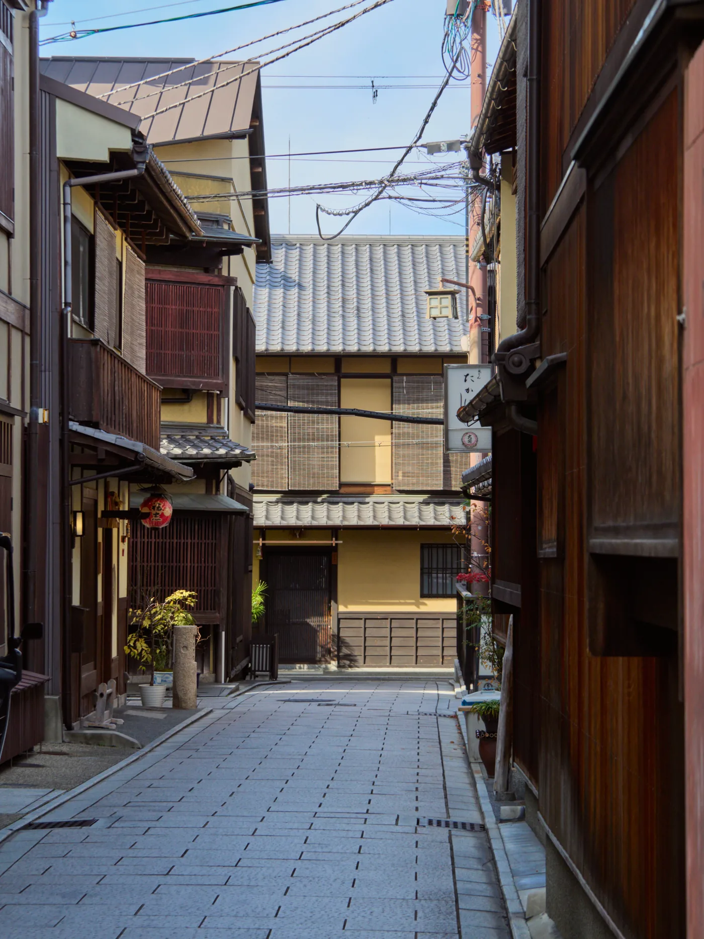 A narrow pedestrian alley in Kyoto, lined with wooden machiya townhouses in the early morning