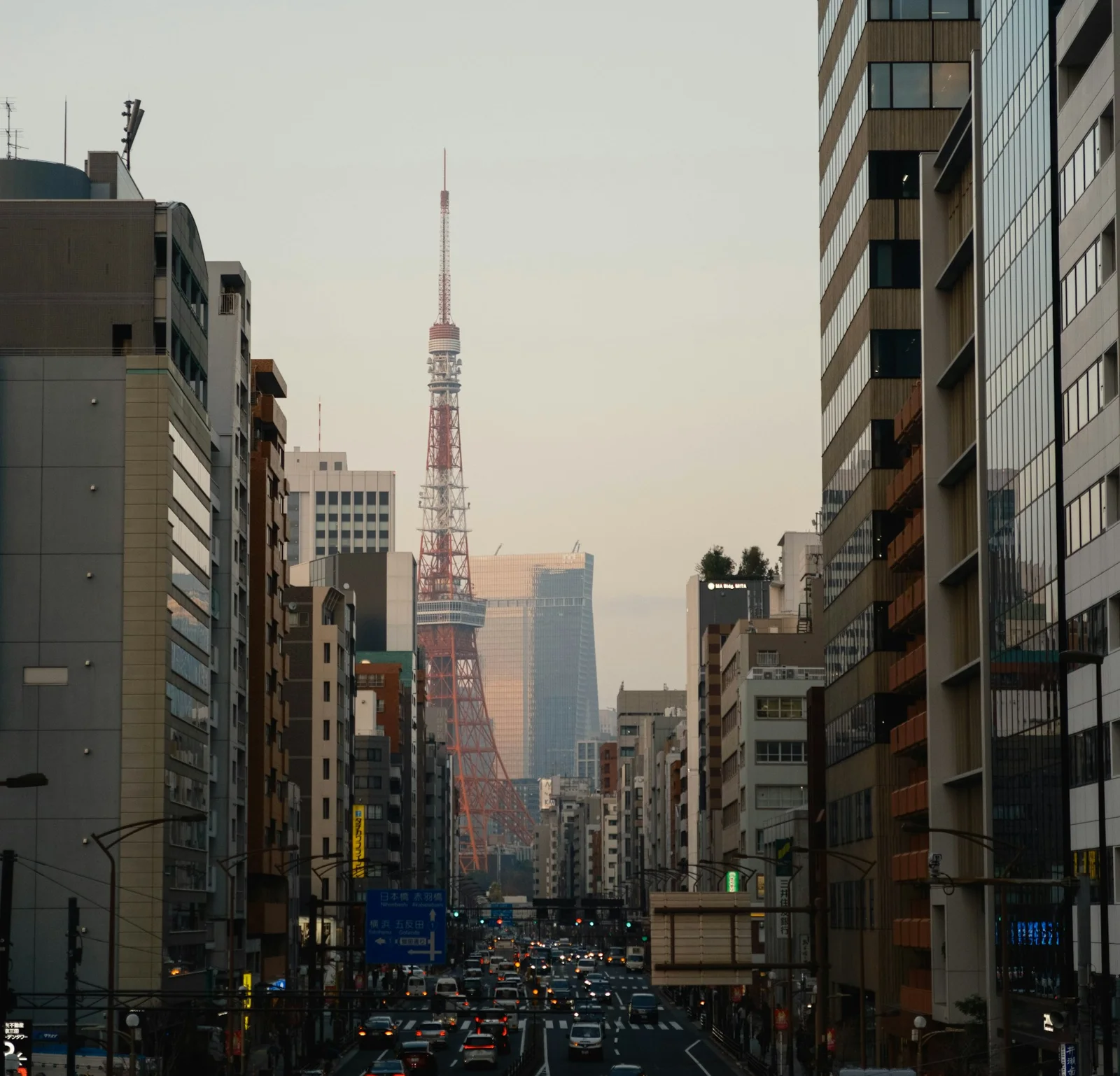 An avenue in Tokyo seen between office buildings, with Tokyo Tower in the haze beyond the traffic