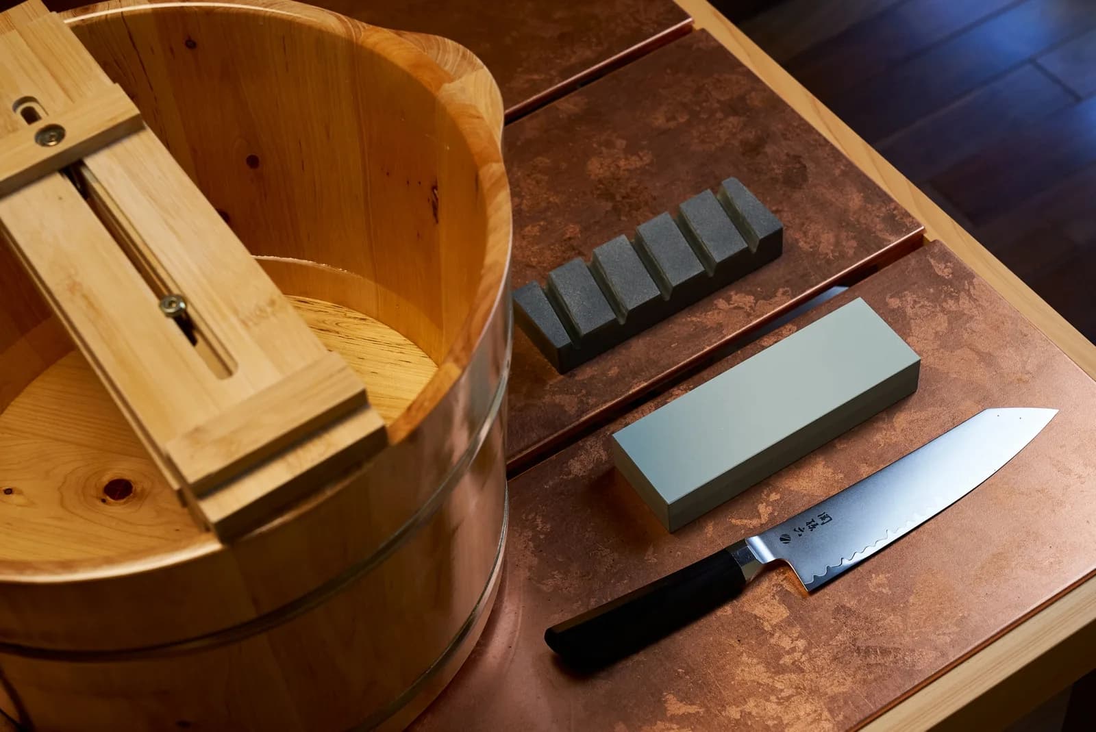 The full kit on the counter: the wooden basin with its stand across the top, a coarse stone, a finishing stone and a knife