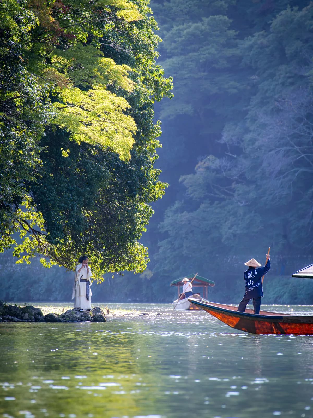 A player in white robes on the rocks at the left bank, a boatman poling a covered boat at the right, the gorge behind them